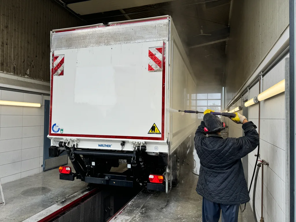 Eine Person reinigt einen LKW mit einem Hochdruckreiniger in der Halle.