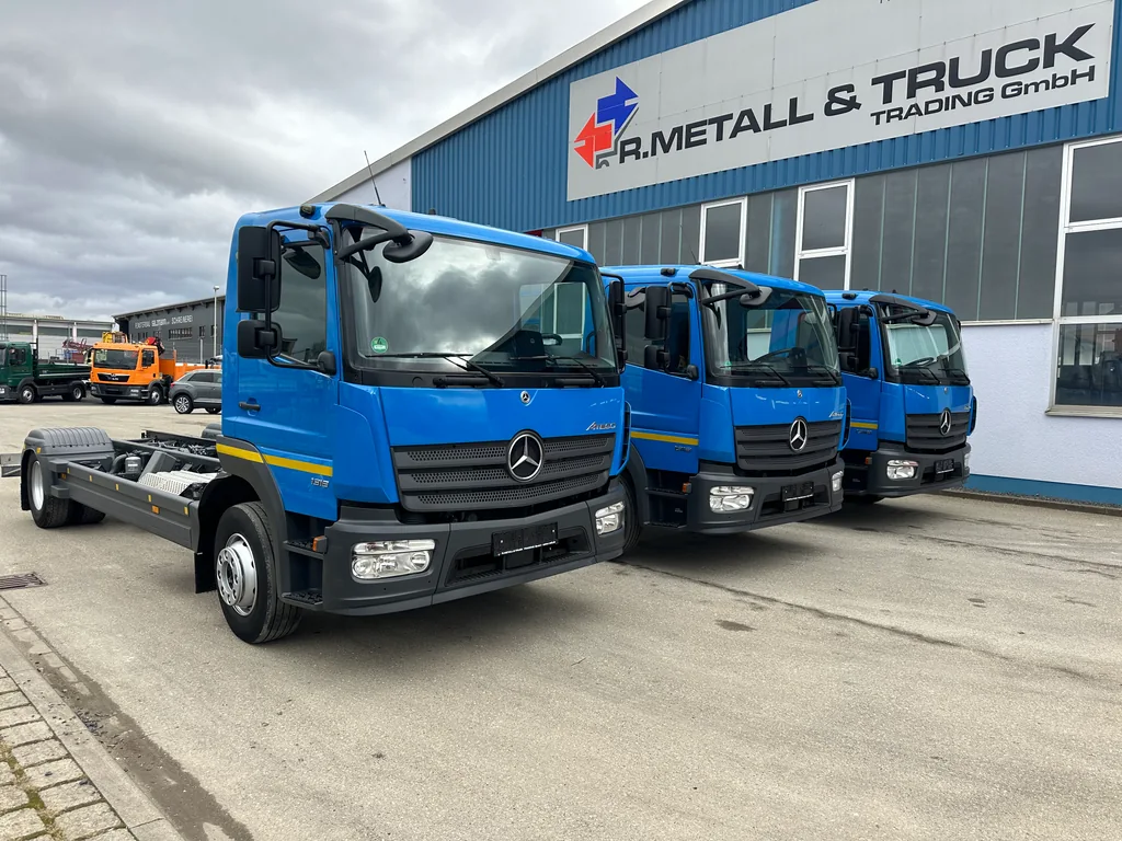Drei blaue Mercedes-LKW vor der Halle von R. Metall & Truck Trading.