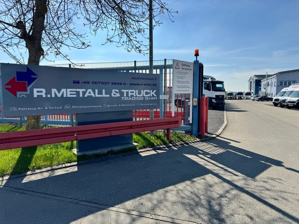 Einfahrt zum Betriebsgelände von R. Metall & Truck Trading mit Firmenschild und Blick auf den Hof.